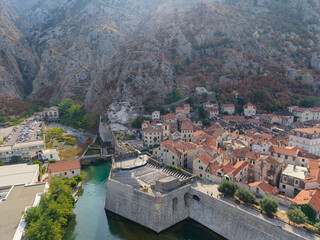 Kotor old town fills Montenegro valley, where pale stone buildings and terracotta roofs meet fortified river walls. Dramatic rocky mountains form striking backdrop to this historic Adriatic city. © Pasha