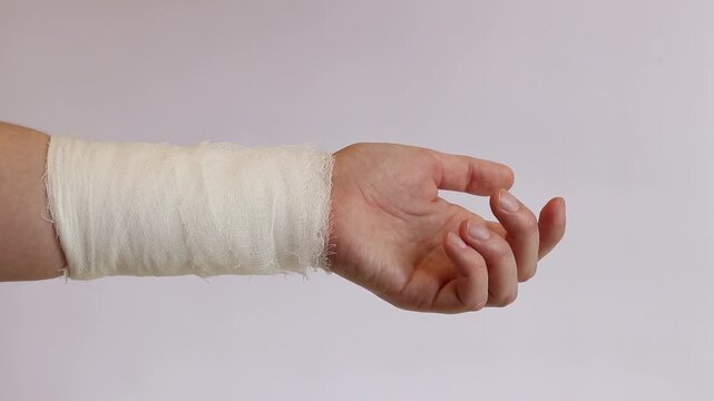 Wrist bandaged with a medical bandage on a light neutral background. A person with a hand injury and a gauze bandage, isolated on a white background. First aid, applying a bandage