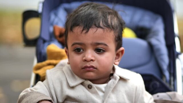 Indian baby exploring park while sitting in stroller during autumn day