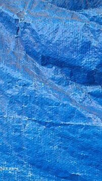 close-up vertical view of a blue plastic tarp texture with visible woven patterns, folds, and natural creases
