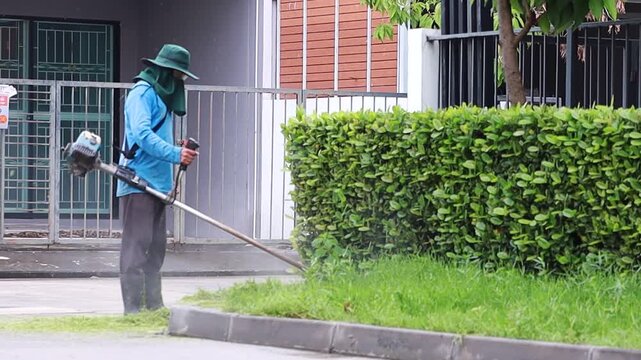 Asian male worker cutting grass with a gasoline lawn mower in a residential area