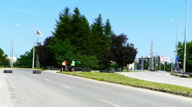 Tilt-shift timelapse wide shot of sport cars speeding past race marshals waving flags on a closed city road. Miniature effect fast motion panorama of an urban motorsports event outdoors.