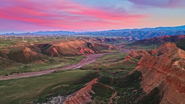 Aerial view of a dramatic pink sunset sky over rugged mountain valley and dry riverbed along S101 highway in Xinjiang, China.