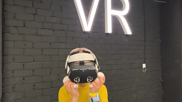 A boy in yellow T-shirt immerses himself in virtual reality. Playing virtual reality game with headset. A party children's center. Modern technology, VR games, and digital entertainment for children.