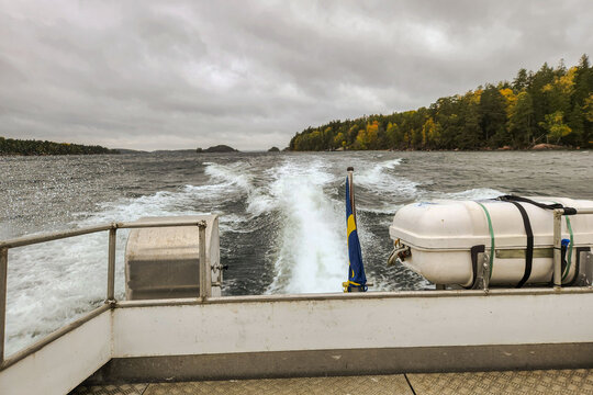 Close up view of water taxi leaving foamy wake on Baltic Sea against background of forested islands. Sweden.