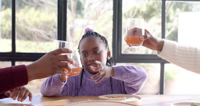 Family with female child picking glass while adults raising drinks at wooden table for toast