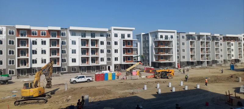 CALGARY, CANADA - 28 MAY 2026: Multi-story residential apartment block construction site with yellow excavator and foundation piles