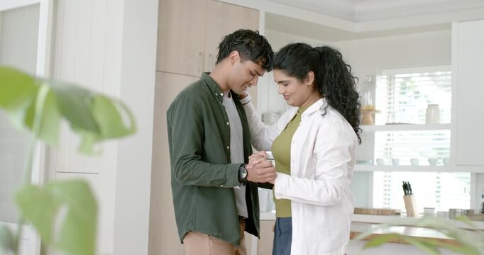 Indian couple holding hands, leaning foreheads, embracing and swaying in kitchen showing love