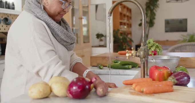 Mature African American woman in scarf rinsing carrots under running tap moving to colander washing