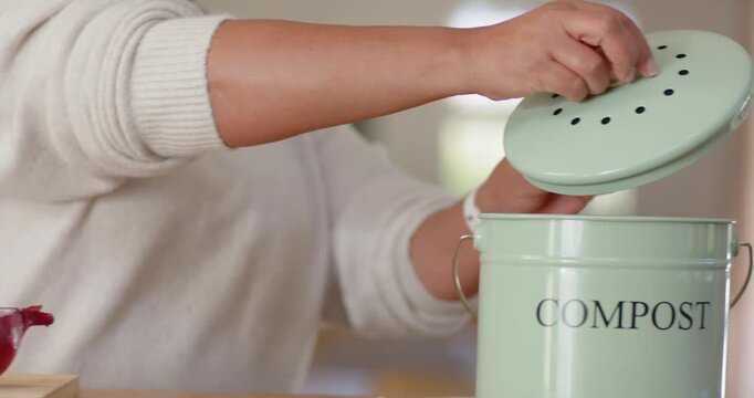 Knife is trimming onion on counter and hands are placing scraps into compost pail for composting