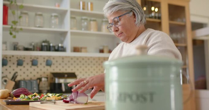 African American woman prepping vegetables, chopping red onion on board at counter, compost can