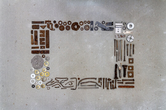 A frame of various old rusty bits and pieces arranged on a concrete surface. Old rusty nuts, bolts, nails and other parts flay lay on gray background.
