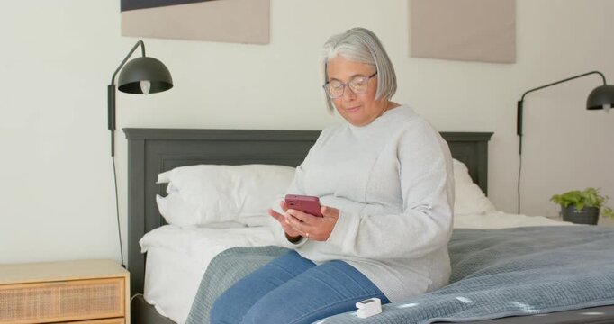 African American senior getting alert and reading messages on phone in bedroom, smiling