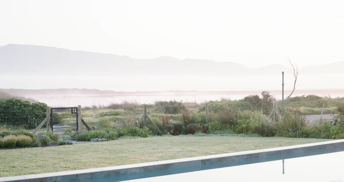 Coastal backyard lawn and fence are clearing as morning light is lifting mist revealing ridge