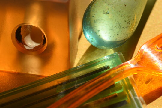 close-up shot of translucent orange and green plastic objects mixed with a glass marble under warm sunny light. Artistic geometric background with reflections.