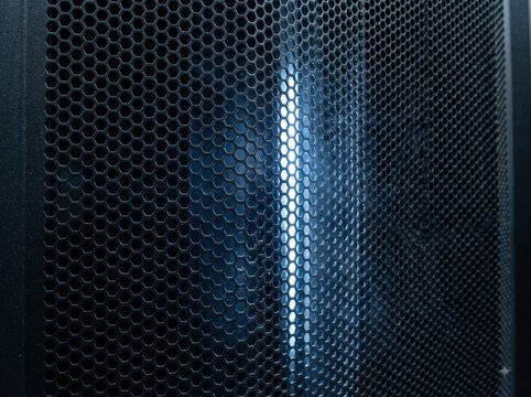 Black perforated metal mesh with hexagonal holes and a vertical streak of glowing blue light, industrial texture and technology background