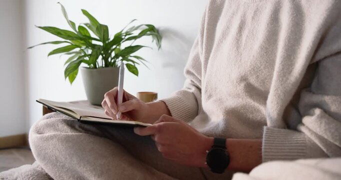 Adult is settling journal and placing pen tip, then is writing entries on lap at home