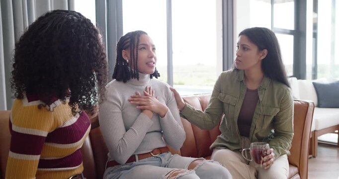 Diverse women friends consoling center woman on leather sofa after woman revealing news, mug aside