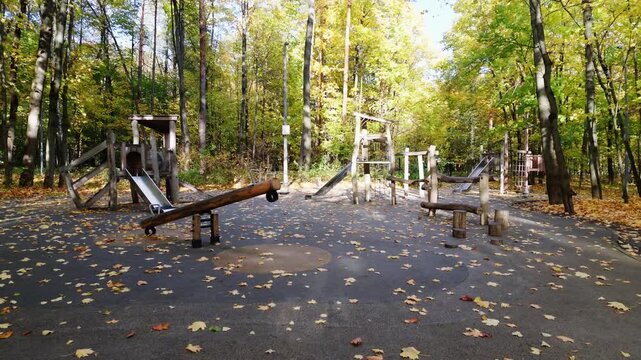 Empty wooden playground with slide and seesaw covered by fallen leaves in an autumn park.