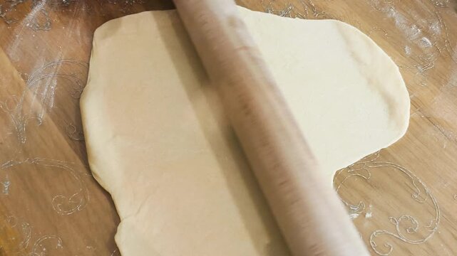 Hands using rolling pin to flatten dough for pastry or bread making. Skilled hands using rolling pin to flatten dough for pastry or bread making on rustic board, creating perfect culinary base.