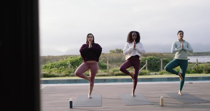 Diverse women starting, moving into tree pose on yoga mats on deck by pool practicing balance