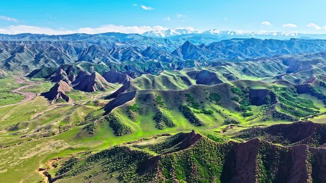 Aerial view of rolling green hills and distant snow-capped mountains along scenic S101 highway in Xinjiang, China.