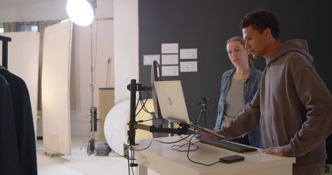 Diverse duo reviewing playback selecting shots woman DSLR pointing at screen, man typing