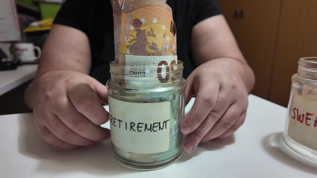 Hands place banknotes into a labeled jar. Label reads "RETIREMENT." Another jar sits nearby. Simple, clear action suggests saving for future. Ideal for financial or retirement planning visuals
