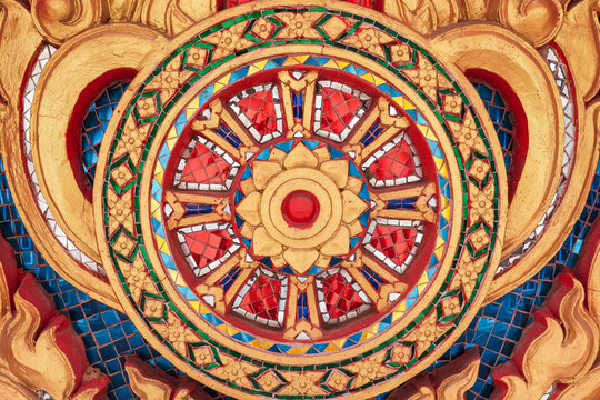 Detailed Thai temple wall pattern featuring golden Dharmachakra wheel adorned with colorful glass mosaic. 
