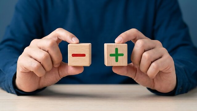 A person holding two small wooden cubes with a red minus symbol and a green plus symbol, representing the concept of positive and negative choices