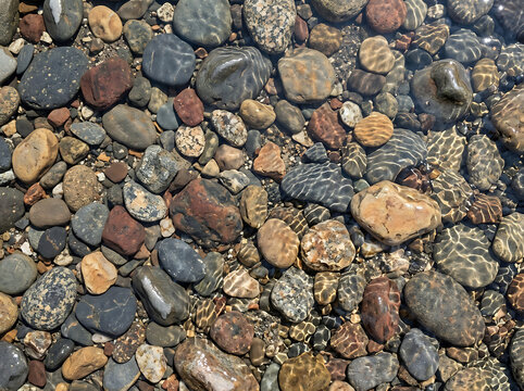 Smooth Gray Pebbles and Textured Natural Stones on Beach Sand Surface