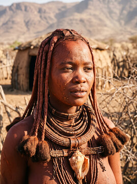 Himba woman adorned with traditional otjize red ochre braided hairstyle and jewelry in Namibia