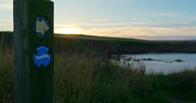 Coastal Path signpost with rugged coastline background at sunset in Eyemouth