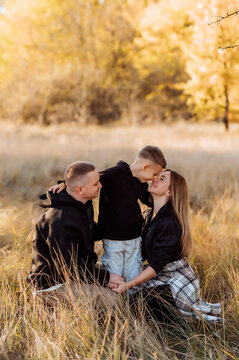 Family of three sitting in a golden autumn field with their young son touching noses with his mother