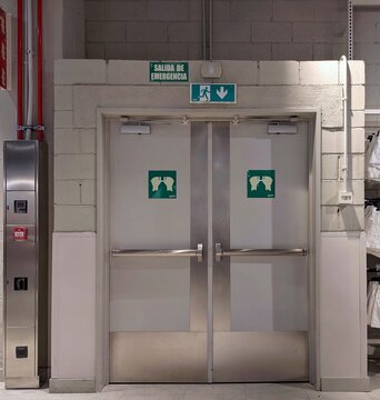 Salida de emergencia con doble puerta con barra antip&aacute;nico horizontal para abrir empujando, junto a un armario met&aacute;lico con equipo contra incendios, en el interior de un edificio de oficinas