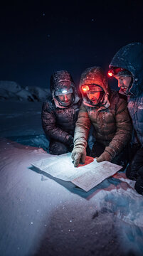 Three Explorers Studying a Map by Headlamp in a Snowy Winter Night Landscape