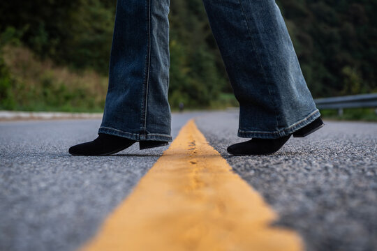 Woman stepping across yellow line on asphalt road, metaphor for crossing boundaries and making decisions
