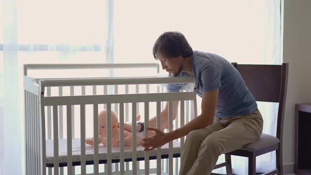 Sleepy father talking to six-month-old son in crib before falling asleep. Concept of parental exhaustion.
