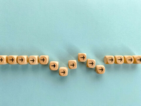 Wooden directional blocks illustrate a change of direction after a distraction and return to the right path representing refocusing on goals, overcoming challenges and business strategy.