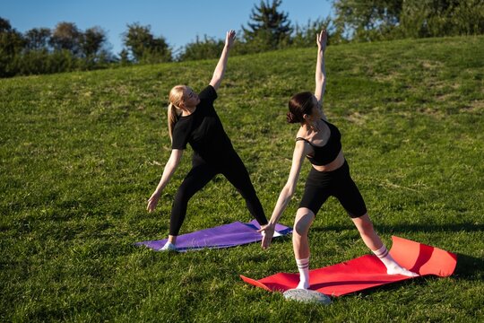 Two women practicing yoga outdoors on a sunny day in the park