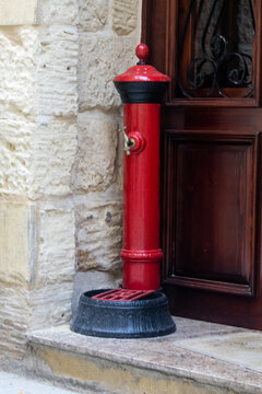 Red Vintage Water Pump Next to Stone Wall and Wooden Door in Mediterranean Alley