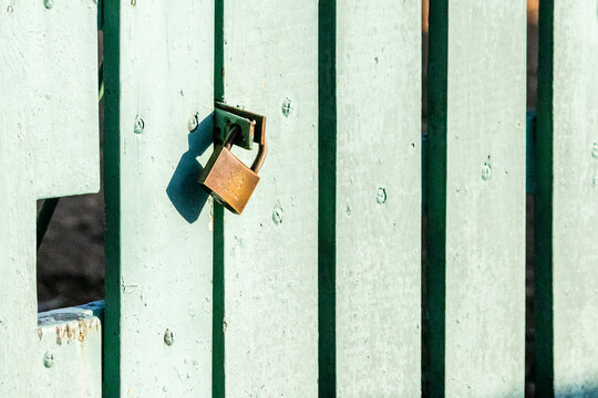 Rustic Brass Padlock Securing Pale Green Wooden Fence Panel Casting Shadow in Sunlight