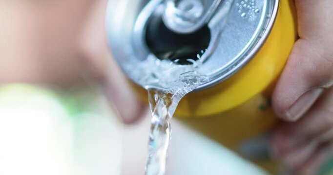 Close-up of a hand pouring a fizzy soft drink from a yellow aluminum can, showing bubbles and flowing liquid, refreshment, carbonated beverages and everyday consumption