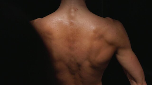 Close-up of technician applying spray tan to woman's lower back and upper thigh in studio under warm directional light, skin shimmering with fresh tanning solution