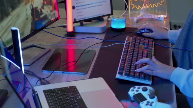 Woman gamer streaming online at neon lit desk typing on mechanical keyboard with mouse while live chat scrolls on monitor in colorful glowing gaming setup late at night