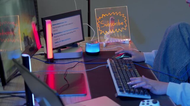 Woman gamer streaming online at a neon lit desk with glowing Subscribe sign and RGB lights while typing on keyboard and using mouse in a dark home gaming studio setup
