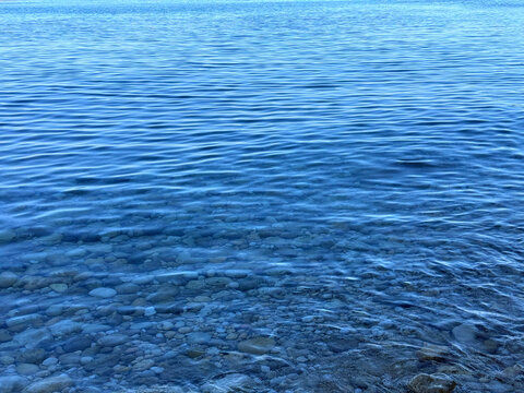 Clear sea water with small ripples on the surface, through which a stony bottom covered with pebbles. 
