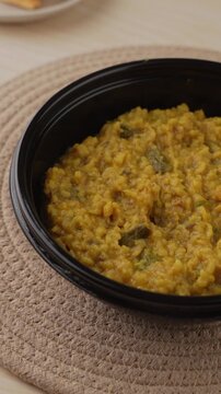 Freshly Cooked Yellow Moong Dal Khichdi with Turmeric Served Hot in a Black Bowl, Close-Up Food Shot.