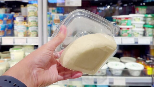 Hand Holding Mozzarella, Suluguni and Burrata Cheese Packages in Supermarket Cheese Section &ndash; Fresh Dairy Products Against Shelves Background
