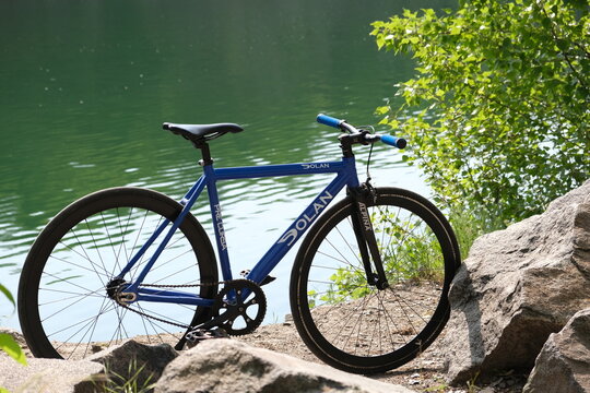 Dnipro, Ukraine - August 7, 2026: Blue Dolan fixed gear bicycle standing on rocks beside green water, showing urban cycling culture, minimalist bike design, active lifestyle and alternative city mobil